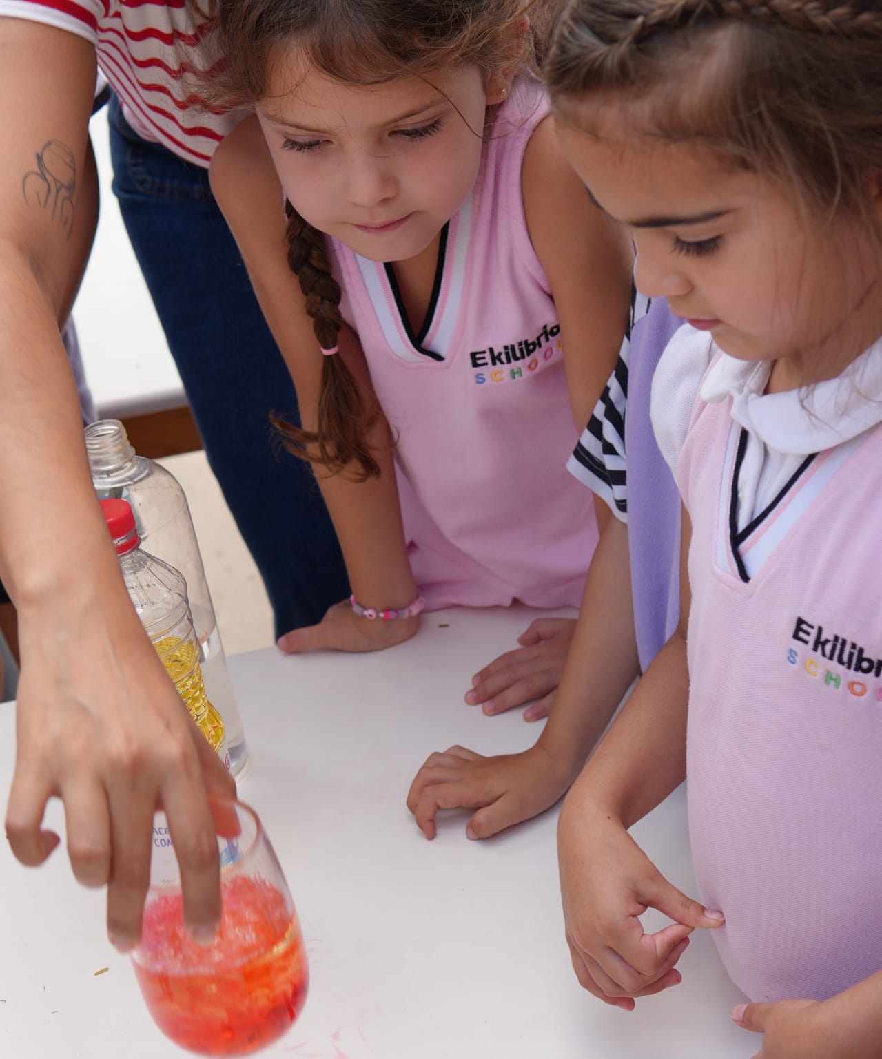 Dos alumnas observan un experimento con un vaso de líquido rojo