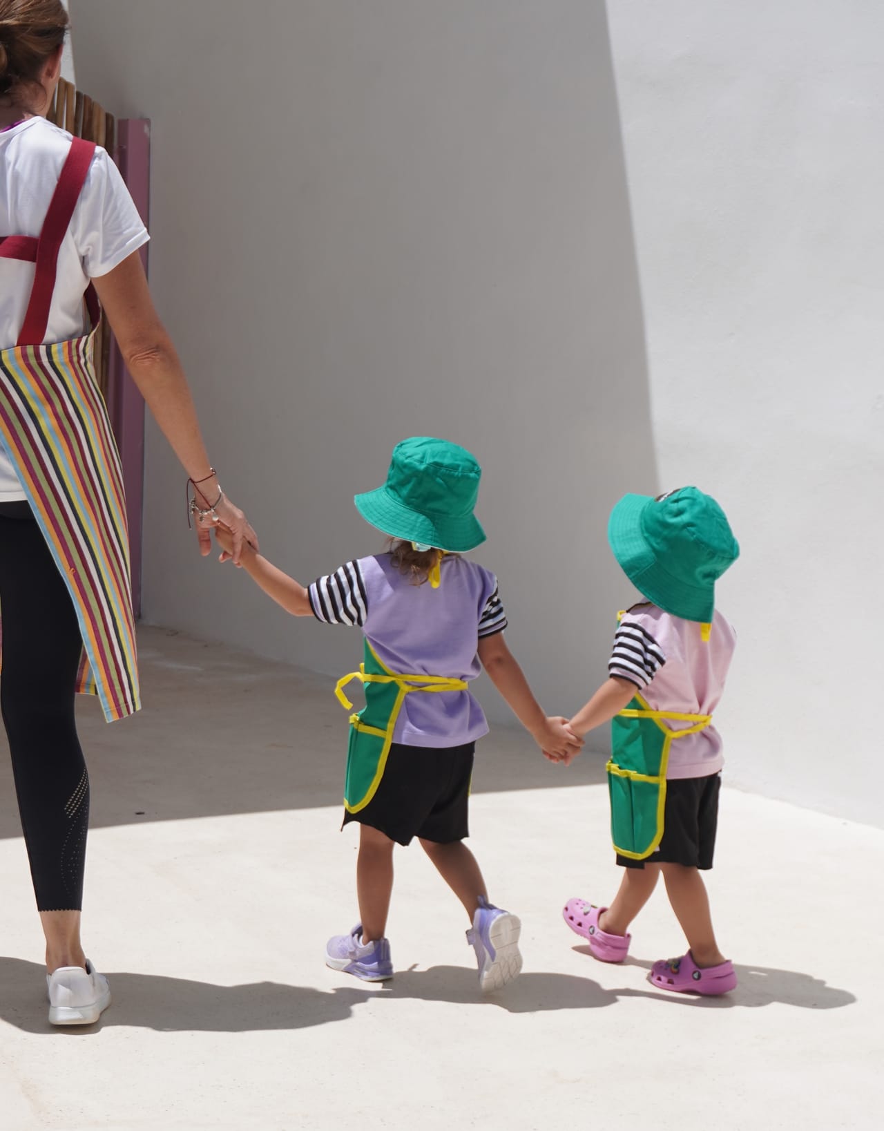 Dos niños de maternal caminan de la mano junto a su maestra